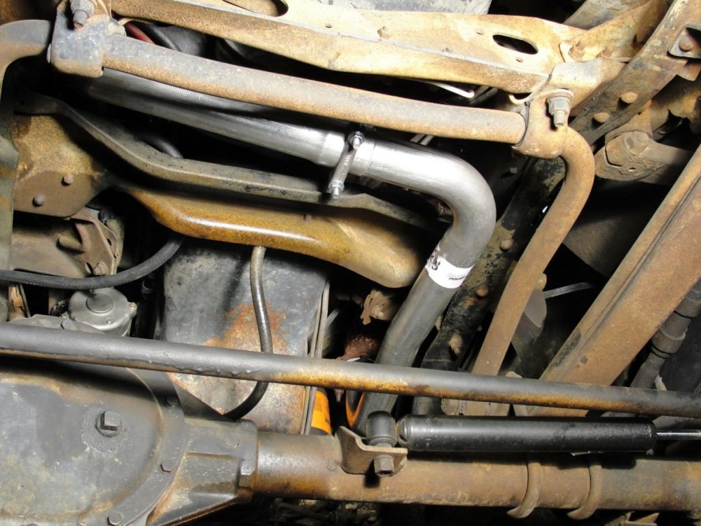 Bolt the exhaust pipe to the new manifold using the supplied gasket and stainless collet locknuts. A heat shield is positioned on the head pipe to help protect the lift pump from direct heat. The factory floating exhaust flange is slipped on the new cross-over pipe and the new doughnut gasket is installed in the manifold before installing the cross-over pipe between the new head pipe and the left side exhaust manifold. The cross-over pipe slips into the new head pipe and is secured using a 2” exhaust U-clamp. The head pipe and gasket is now mounted to the turbo as well.